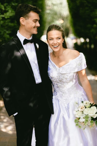 A bride laughs beside her groom on a tree-lined garden path after their ceremony, a Utah wedding