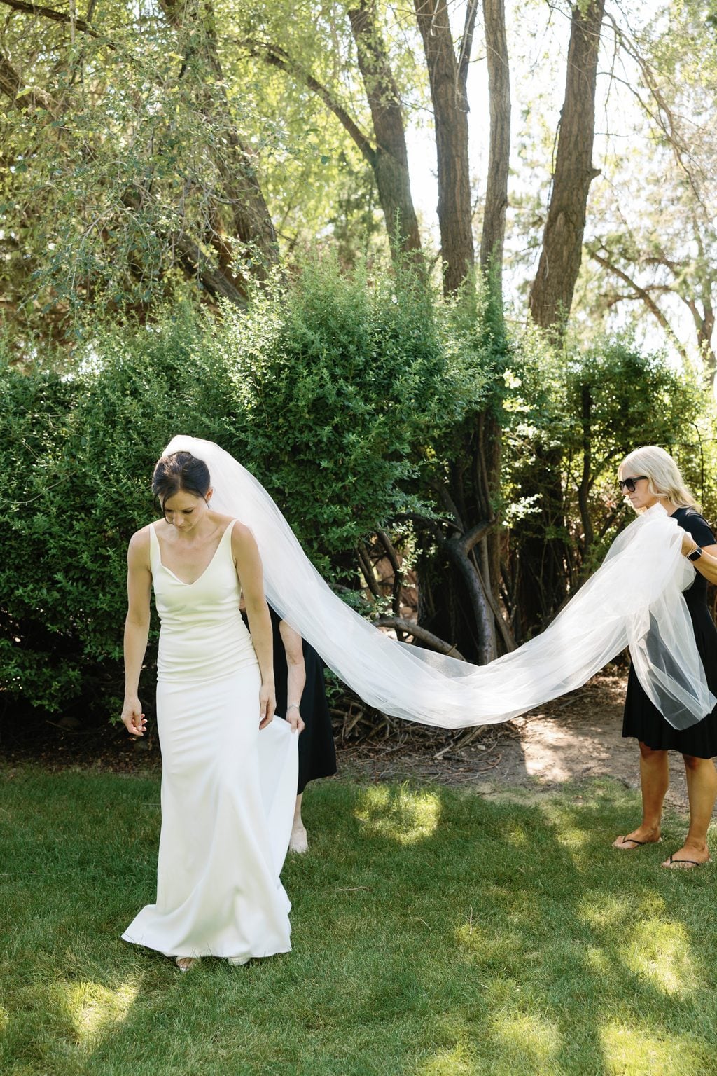 The bride from behind, her long veil trailing across the garden lawn