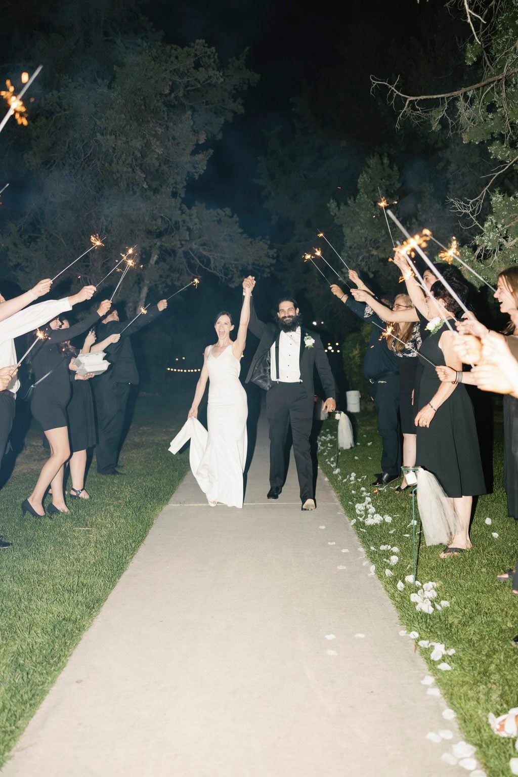 Mallory and Saint's sparkler send-off, arms raised as they walk the lit path